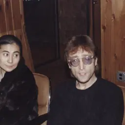 John Lennon i Yoko Ono siedzą w studiu. Yoko w czarnym futrze, John w okularach.