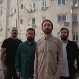 Czterech mężczyzn na tle bloku mieszkalnego, jakby z planety Zeusa.
