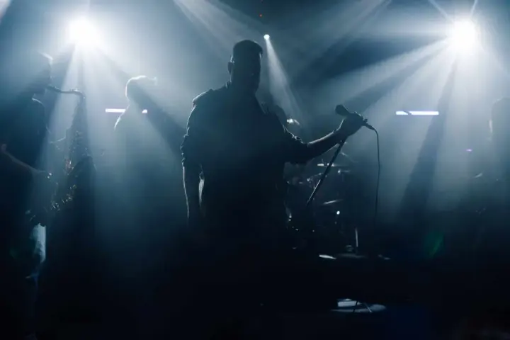 Zespół na scenie, wokalista z mikrofonem, saksofonista. Czy bilety imienne na koncert sprawdzają?