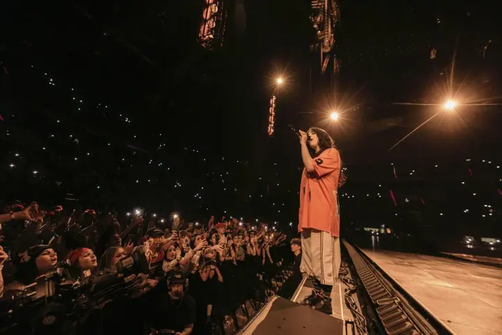 Billie Eilish w Polsce śpiewa dla tłumu fanów, którzy oświetlają scenę telefonami.