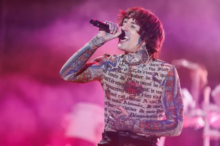 Oli Sykes z Bring Me The Horizon Polska śpiewa na koncercie, ubrany w koszulkę z tatuażami i francuskim tekstem.