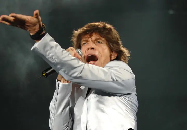 Mick Jagger śpiewa, wykonując swoje legendarne utwory. Wokalista w srebrnej marynarce z mikrofonem w dłoni.