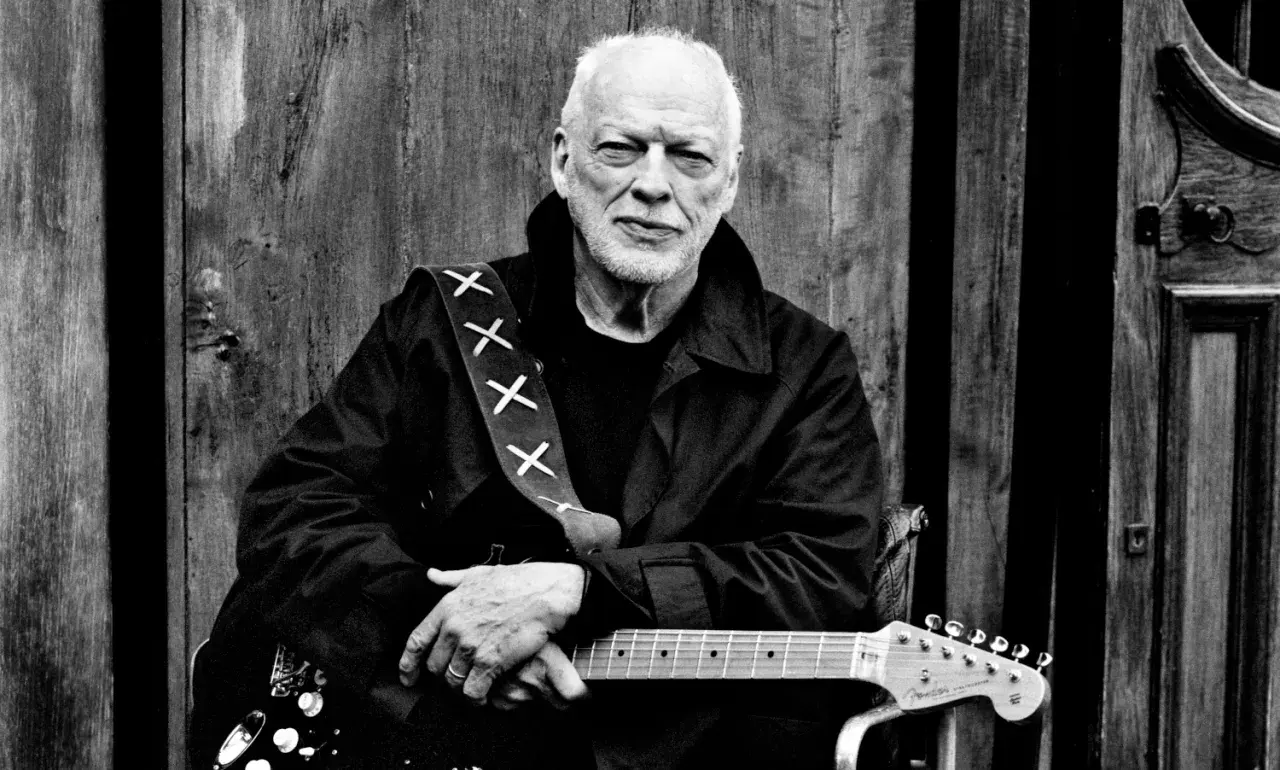 David Gilmour z najdroższą gitarą na świecie, oparty o drewniane drzwi.