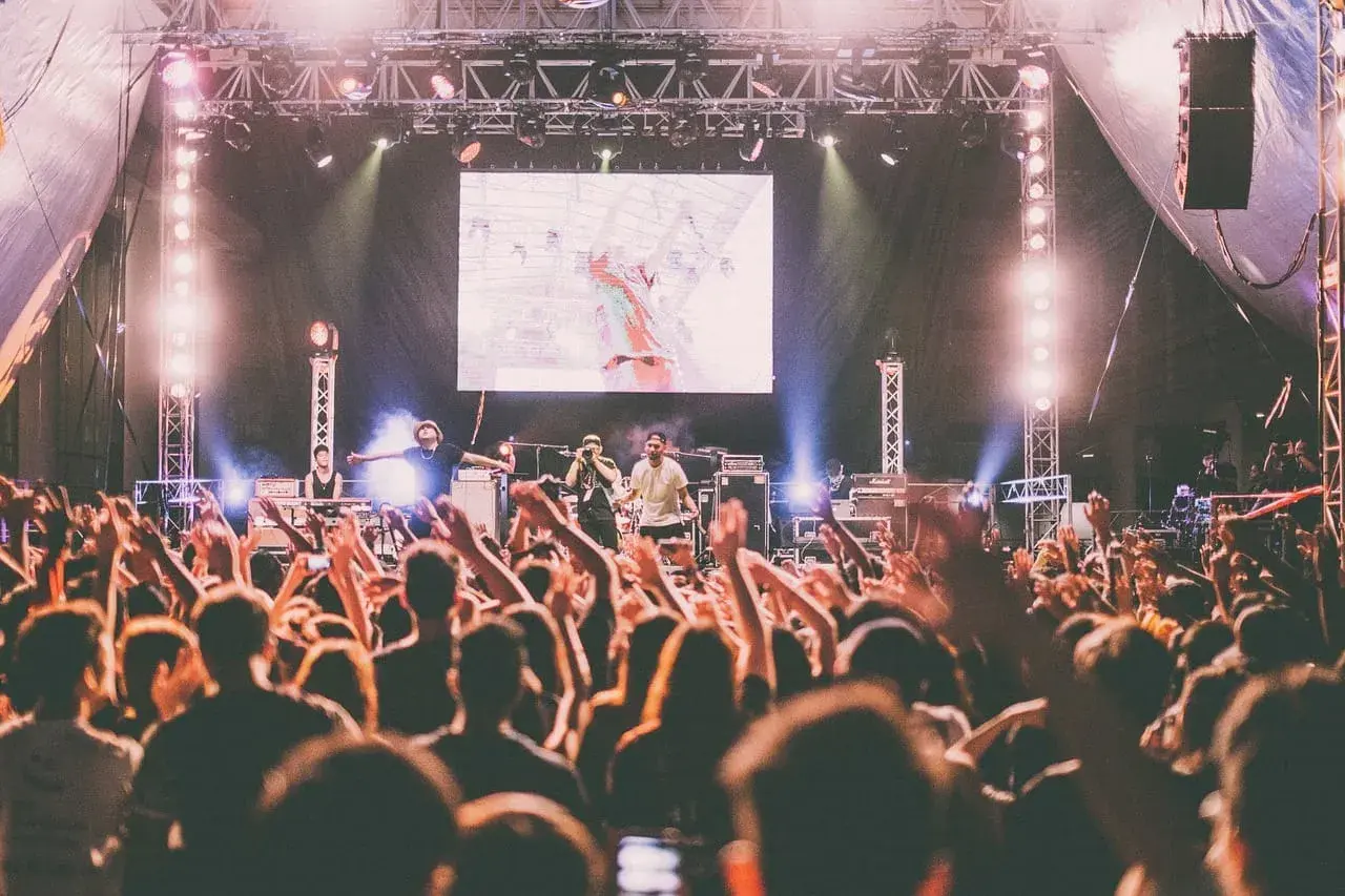 Koncert australijskiego zespołu rockowego. Tłum szaleje, ręce w górze, światła sceniczne.