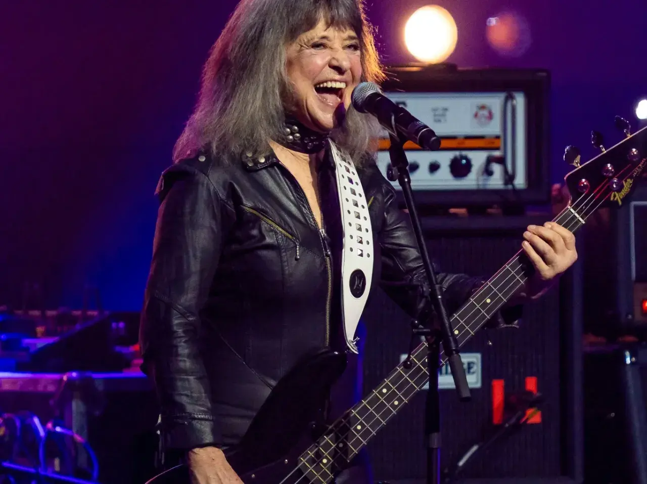 Suzi Quatro, w czarnej ramonesce, gra na basie i śpiewa. Ile lat ma Suzi Quatro? Wciąż pełna energii na scenie!