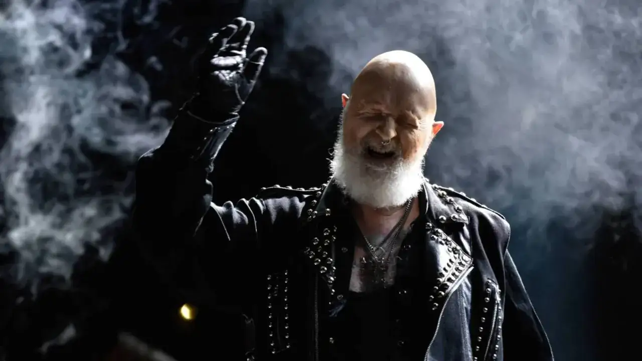 Rob Halford z Judas Priest, w skórzanej kurtce, z uniesioną ręką, w dymie. Jakby przeżywał