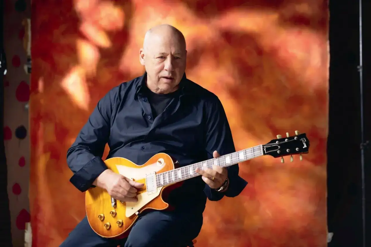 Mark Knopfler, legenda gitary, przygotowuje się do kolejnych koncert&oacute;w. Gra na swoim ukochanym Gibsonie na tle ognistego tła.