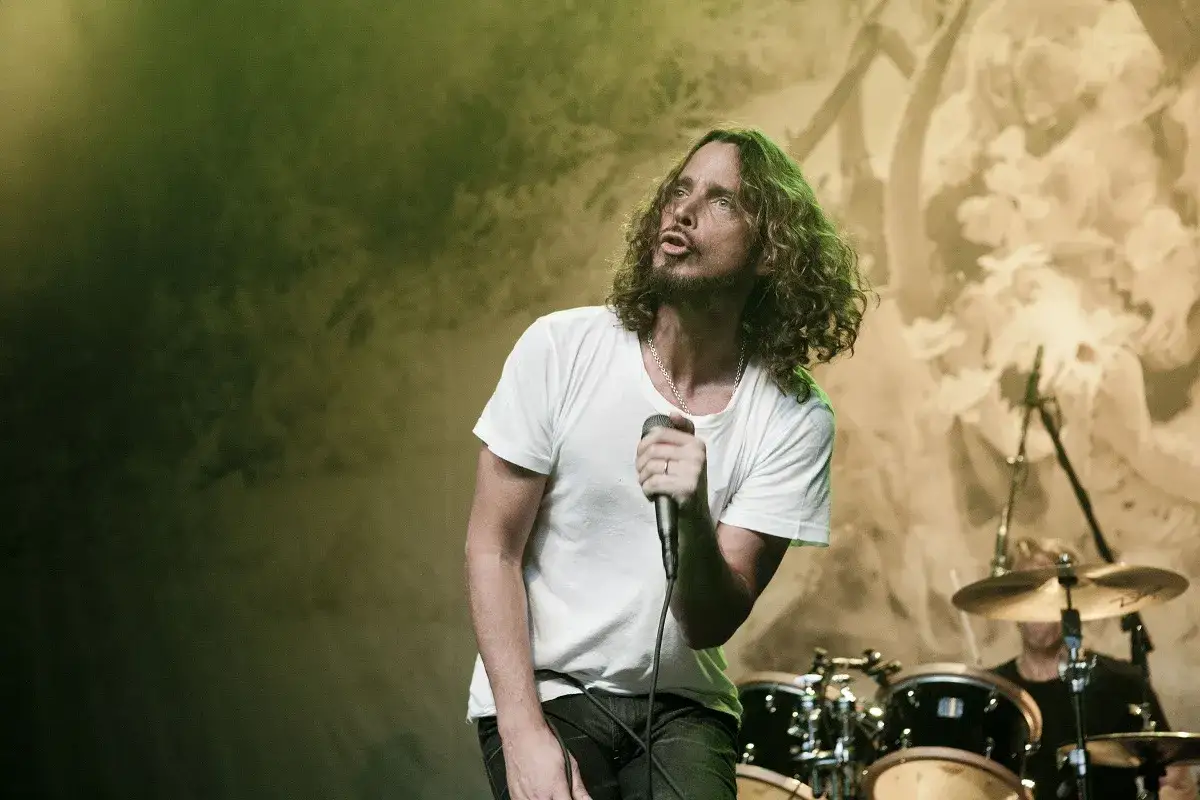 Chris Cornell z zespołem na scenie, w białej koszulce, śpiewa do mikrofonu.