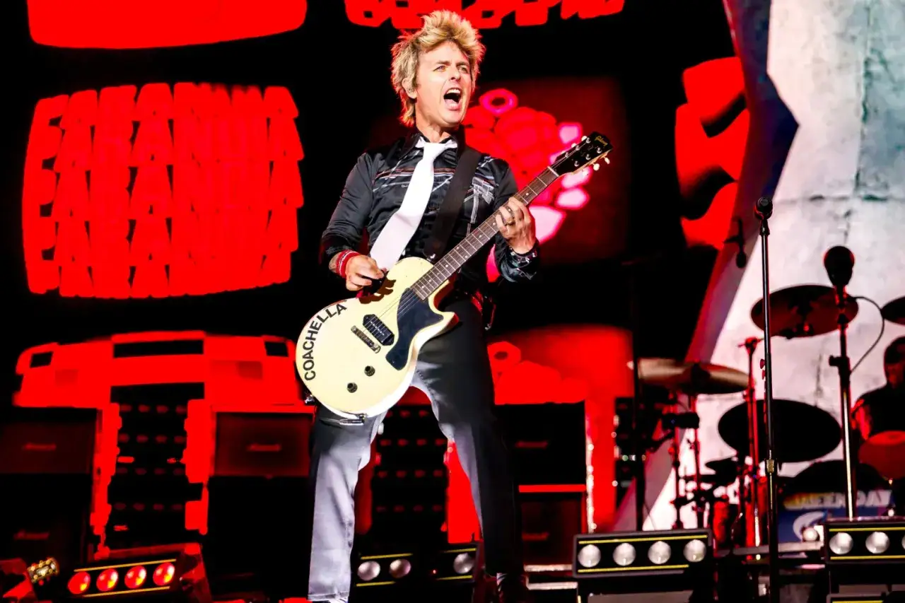 Green Day wokalista Billie Joe Armstrong śpiewa i gra na gitarze na scenie, z napisem 