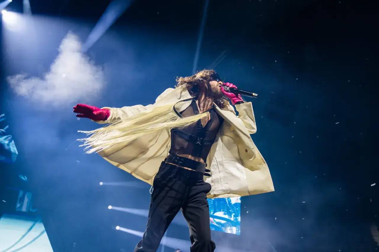 Jared Leto z Thirty Seconds to Mars na scenie, w białym płaszczu i różowych rękawiczkach, śpiewa do mikrofonu.