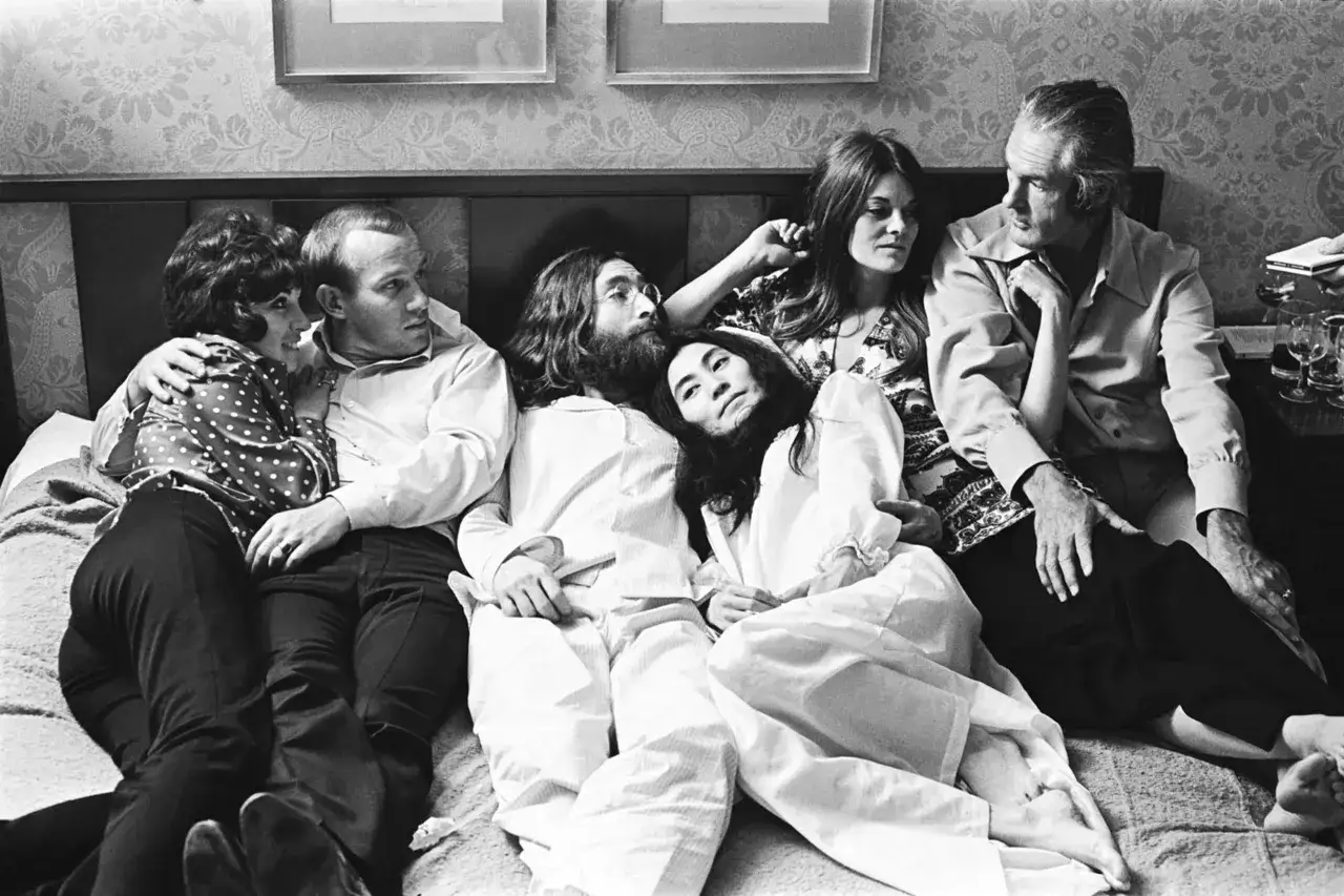 John Lennon i Yoko Ono leżą na łóżku w otoczeniu przyjaciół.